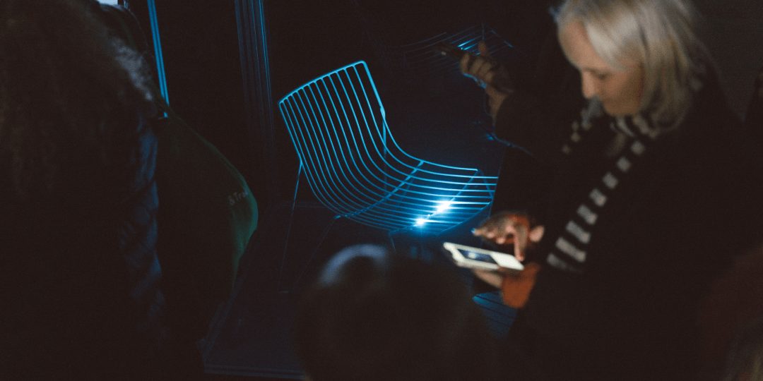 A person looking at her phone with a chair in the background.